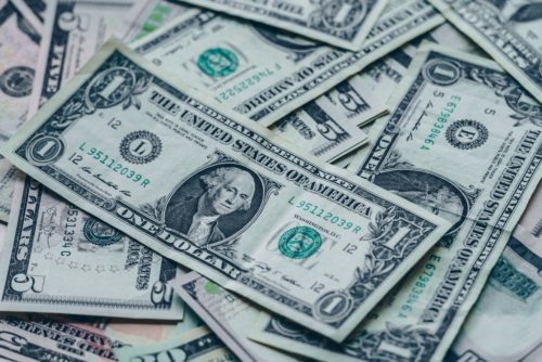 A pile of overlapping U.S. one-dollar bills, featuring a portrait of George Washington and various serial numbers. The bills are arranged at different angles, creating a textured pattern.