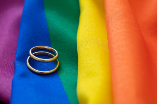 Two gold wedding rings rest on a rainbow-colored fabric, symbolizing LGBTQ+ pride and marriage equality.