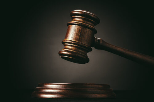 A wooden judge's gavel is raised above a matching sound block against a dark background, symbolizing law, justice, or an impending decision to notify beneficiaries of an inheritance.